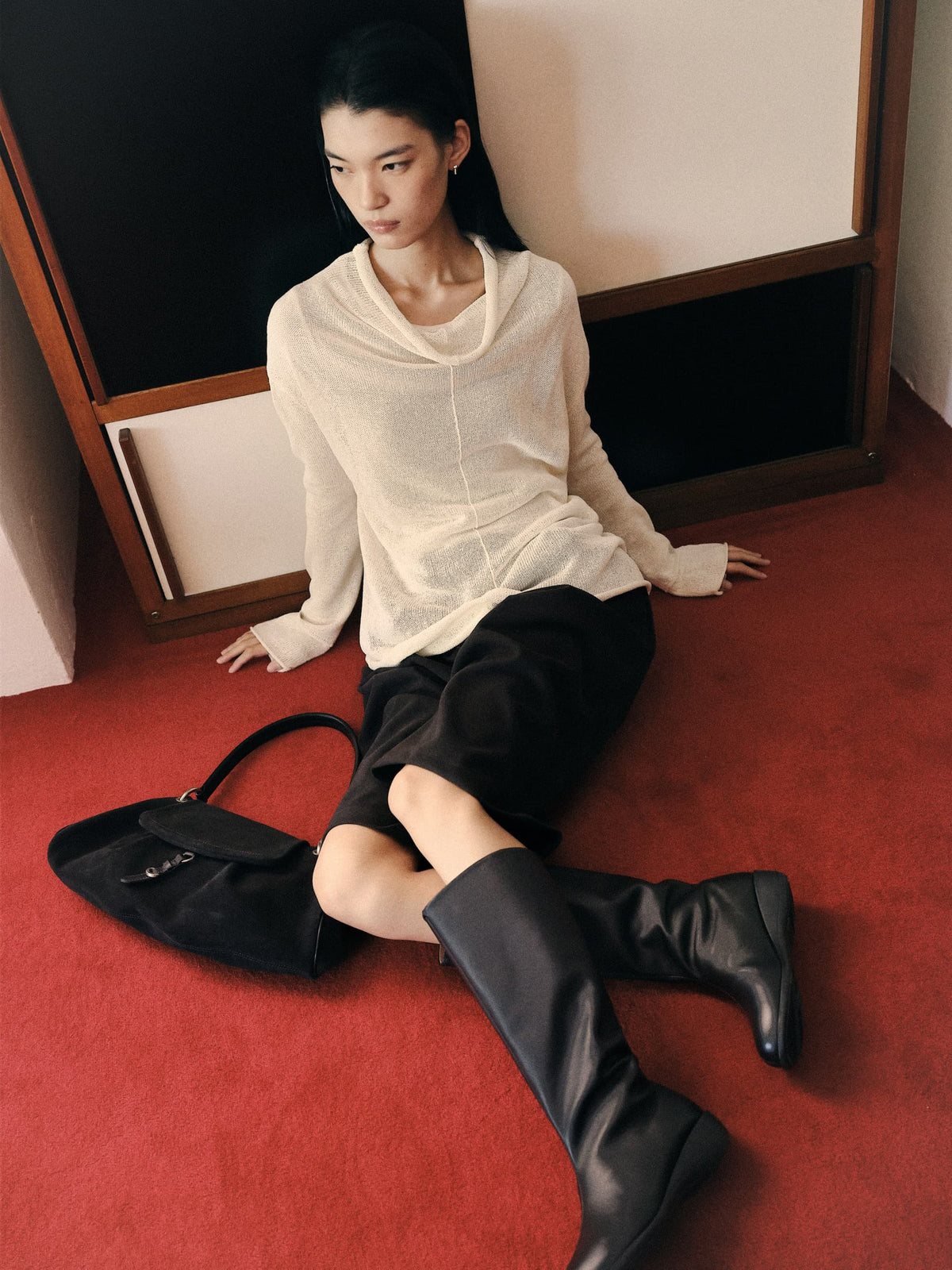 Model seated on a red carpet with a black suede shoulder bag